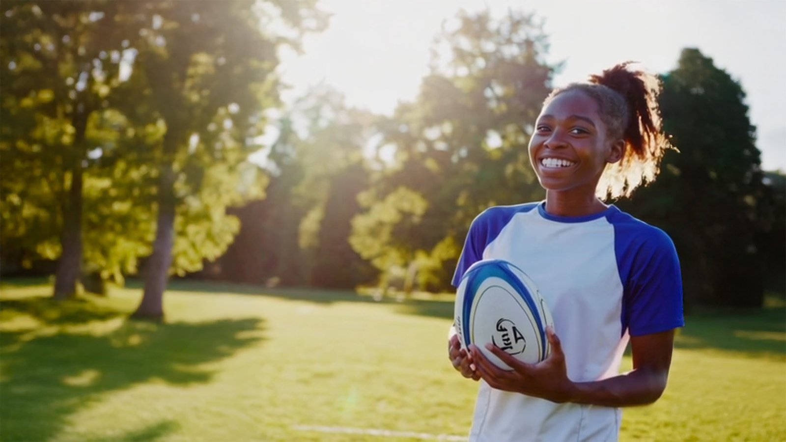 Smiling young rugby player holding a ball on a sunny field — Switch Mentoring helps young people build confidence on and off the pitch.